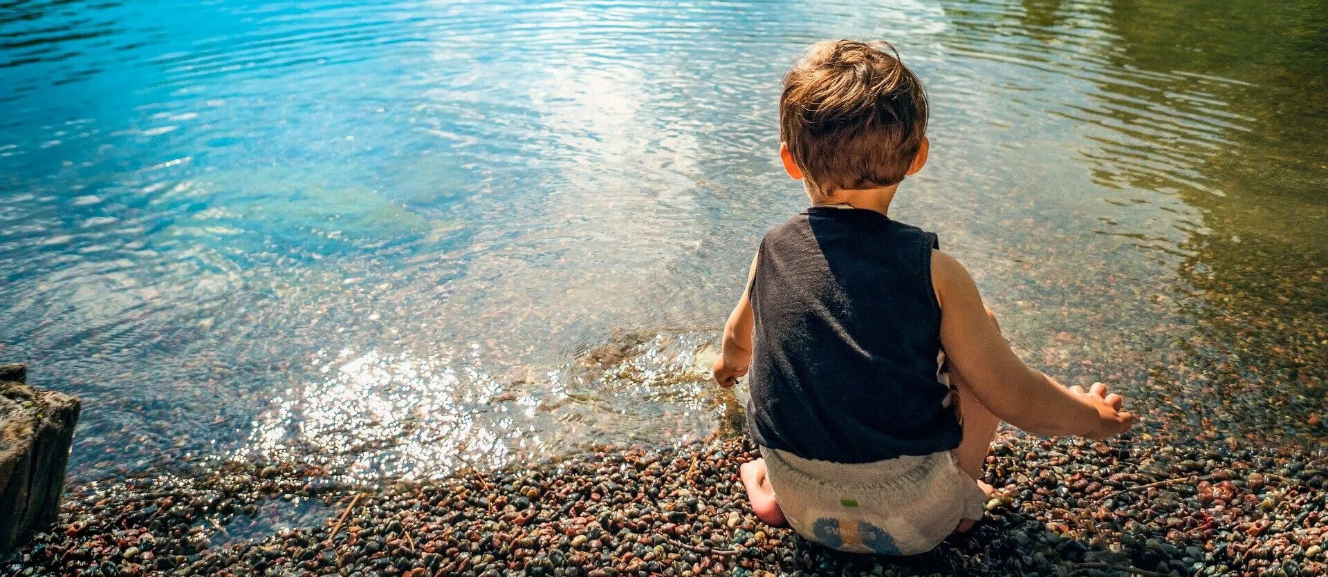 a young boy sitting by the edge of the water.
